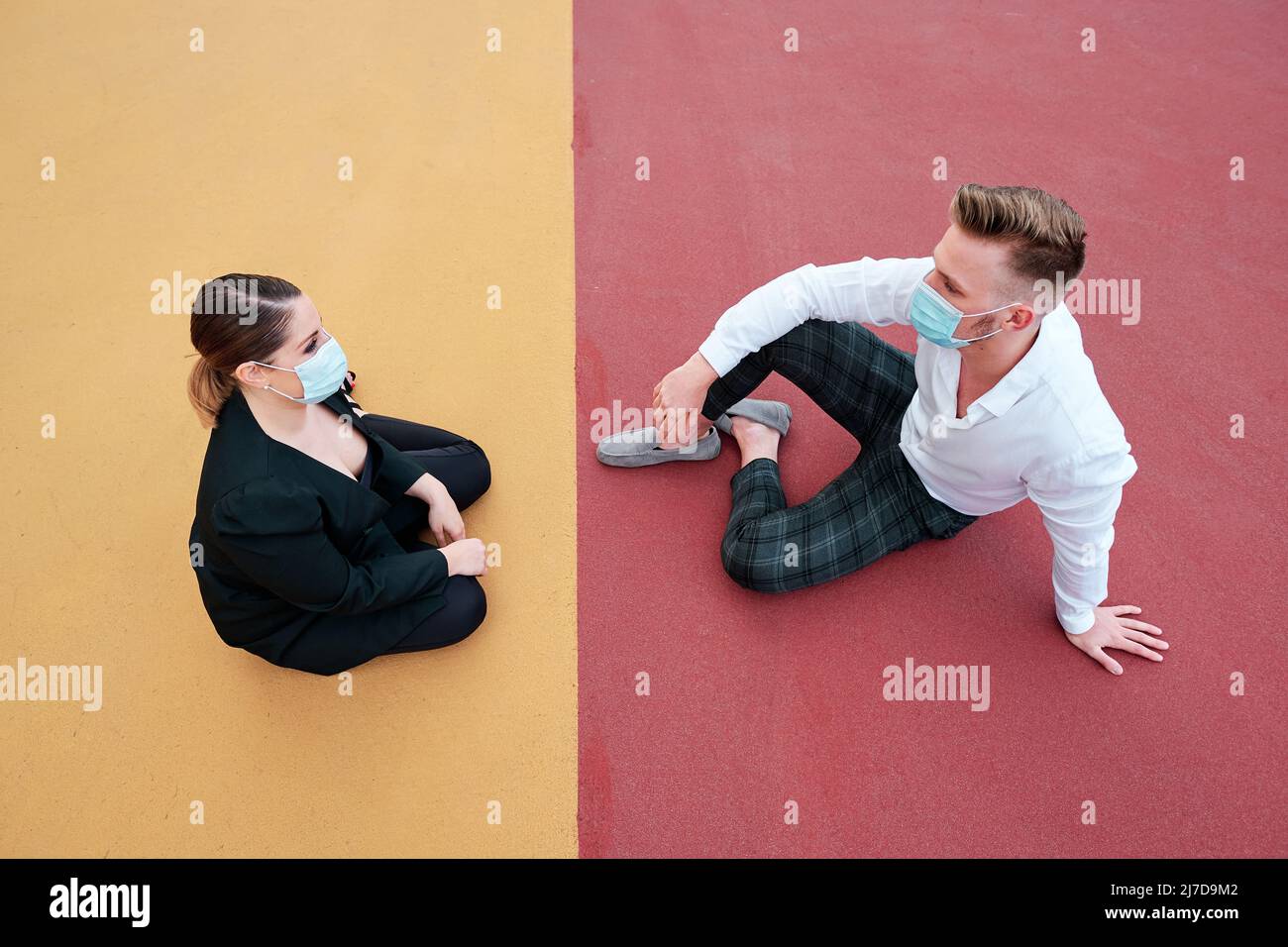 Business people wearing protective masks while sitting together on a different colored floor outdoors. Stock Photo