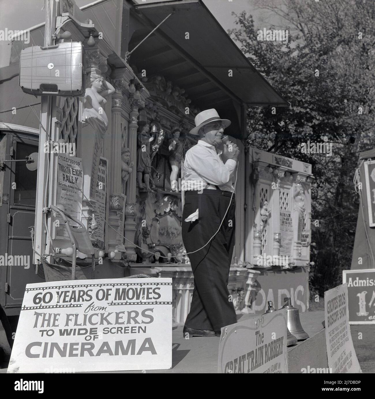 1969, historical, a gentleman on a stand with organ for a Bioscope Show at a Steam Fair, England, UK. The early days of moving pictures saw films shown by travelling fairground showman in portable booths, as well as at  Variety or Vaudeville theatres. A poster infront of the stage says, 'Groves Bros Bioscope Show, The First Public Film in Great Britain', 'The Great Train Robbery', while another says, '60 Years of Movies'. The Great Train Robbery was a 1903 American silent film, 12 mins long, which was a major commerical success at the time. Stock Photo