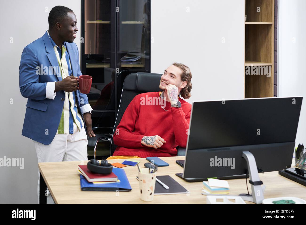 Two multiethnic colleagues talking to each other during work day at office Stock Photo