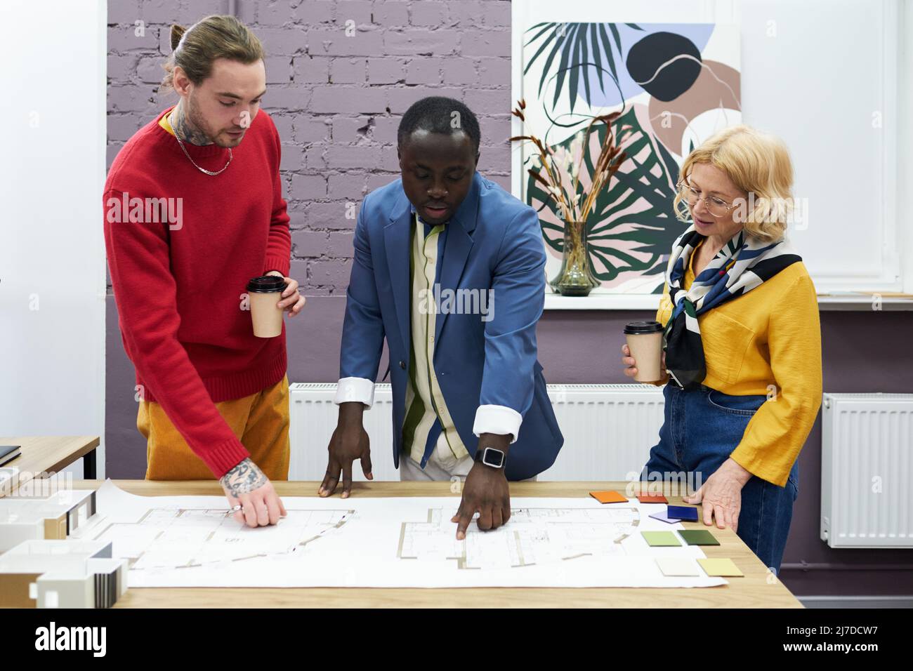 African man pointing at blueprint on table and discussing new project together with his colleagues Stock Photo