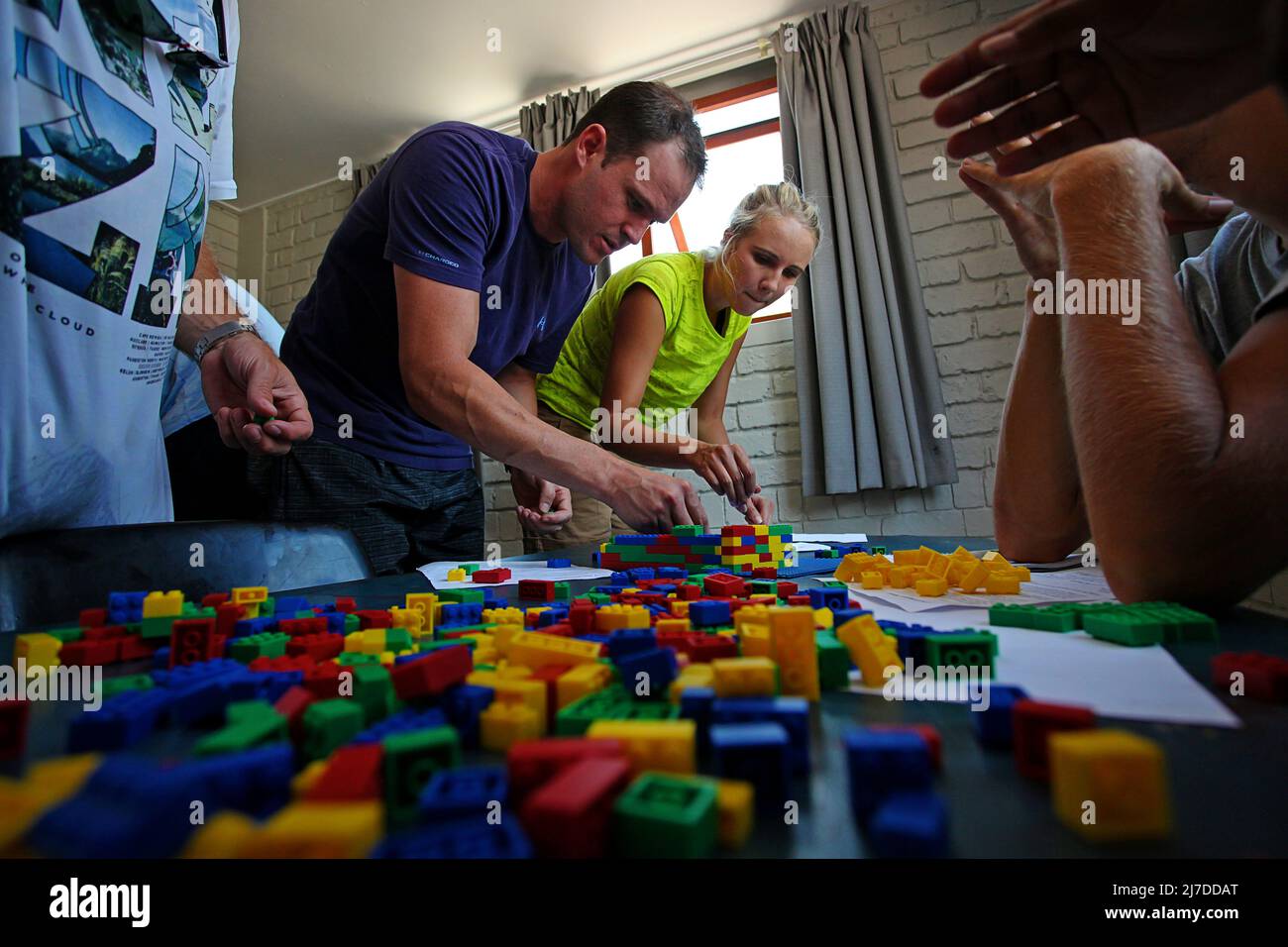 Students gathered around a table at the GSB team-building event, building LEGO structures using specific clues Stock Photo