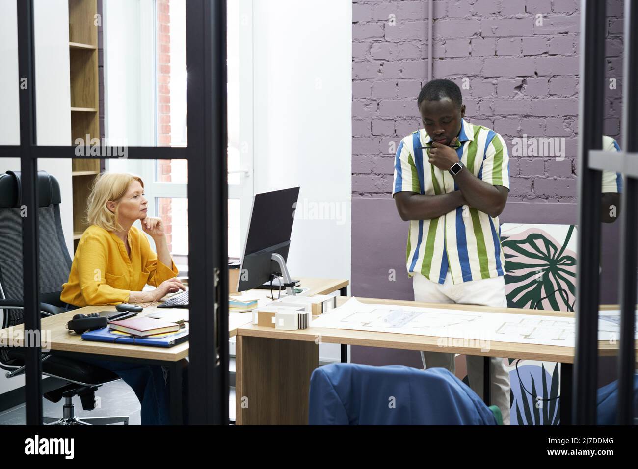 African businessman examining blueprint on table with businesswoman working at her workplace on computer during work at office Stock Photo