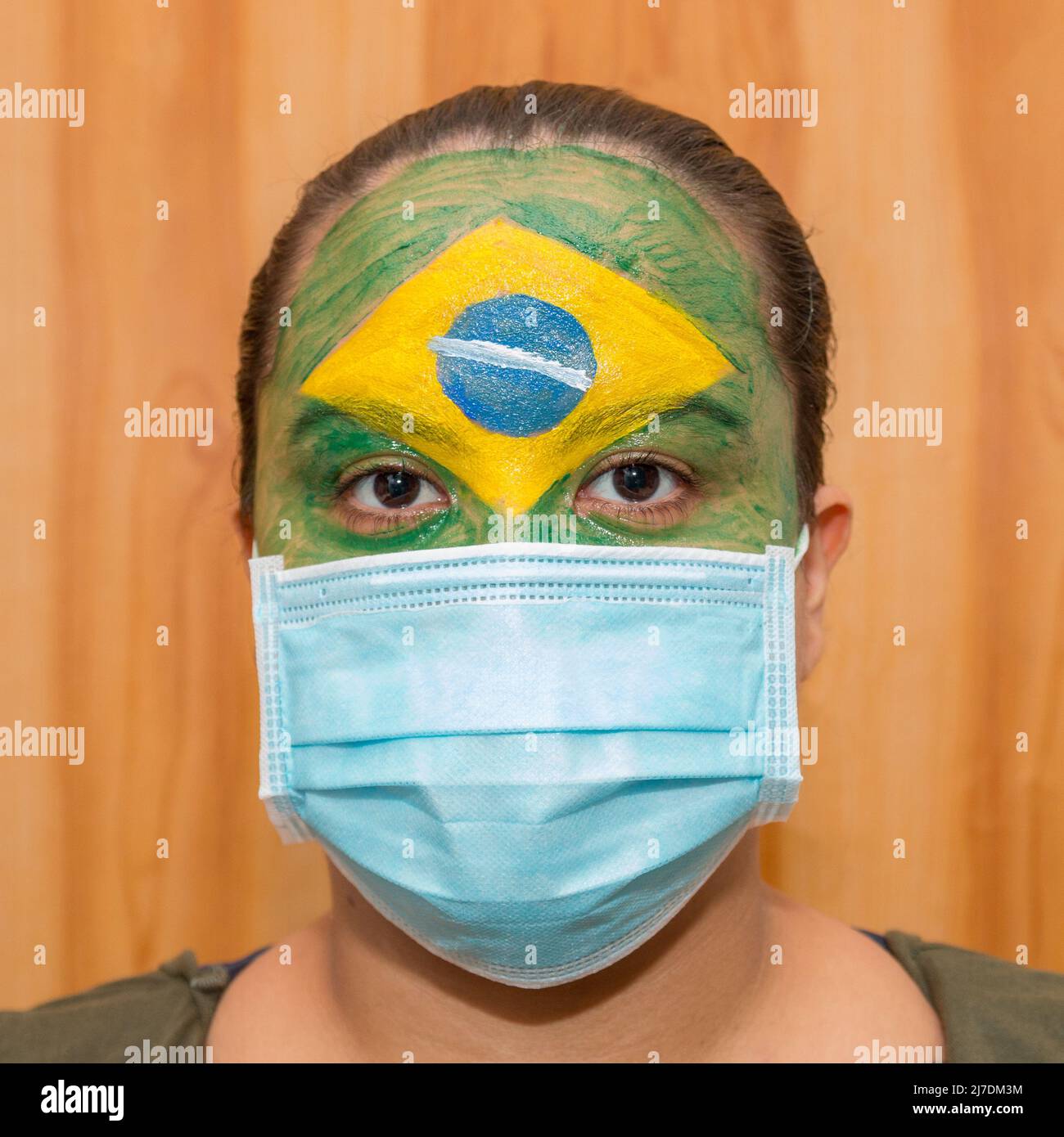 Woman with the flag of Brazil painted on her face with a blue hospital mask in Rio de Janeiro. Stock Photo