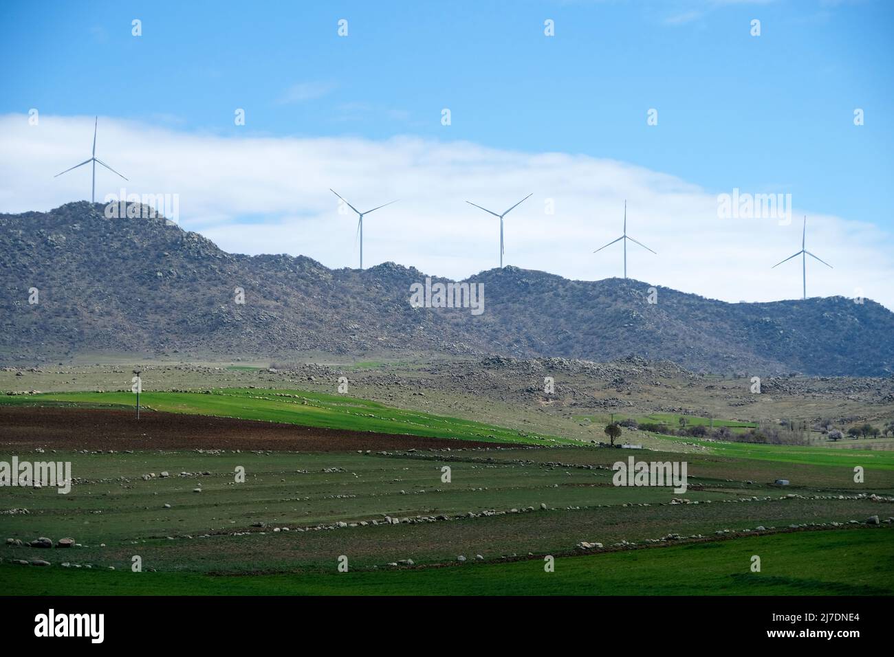 windmills generating electricity on farmlands and hills ahead. Stock Photo
