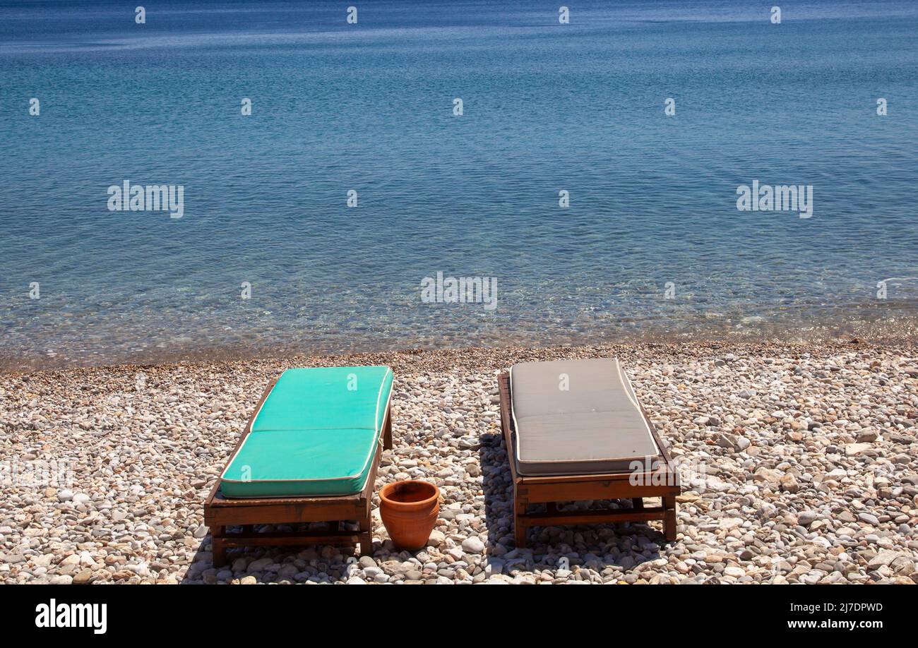 Two empty sun lounges on a small stone beach by the sea. Holiday concept. Stock Photo