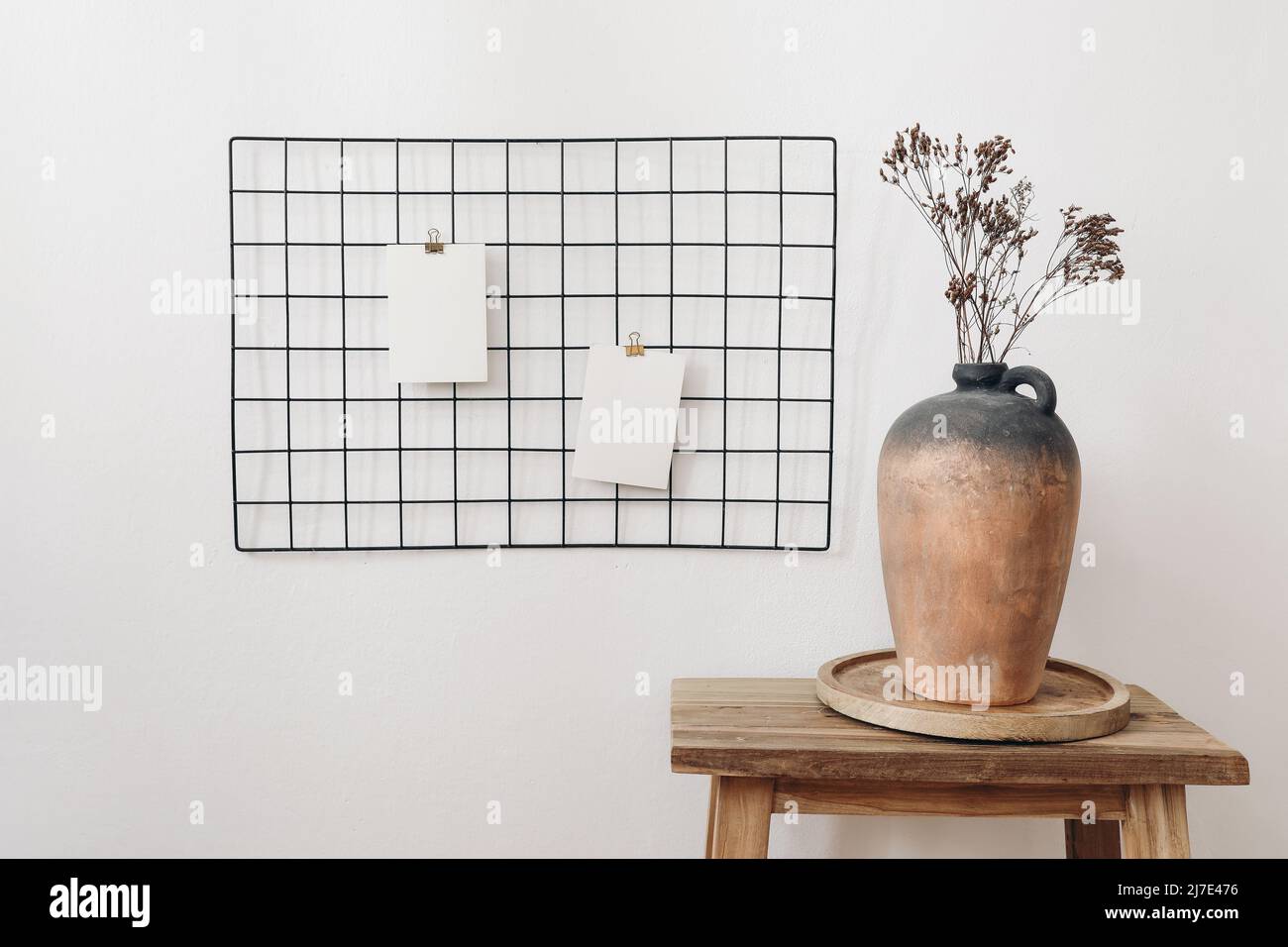 Rustic clay vase with dry hypericum bouquet on wooden table. Black metal mesh noticeboard, bulletin board with blank memo cards mockups. Elegant home Stock Photo