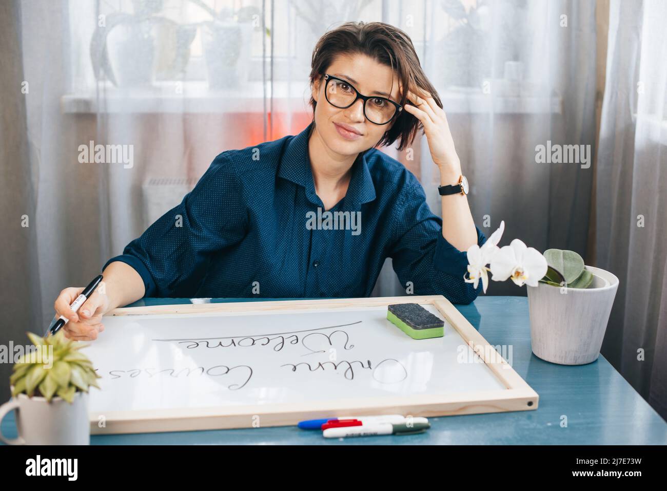 Teacher posing sitting at desk looking at camera writing sentences on a