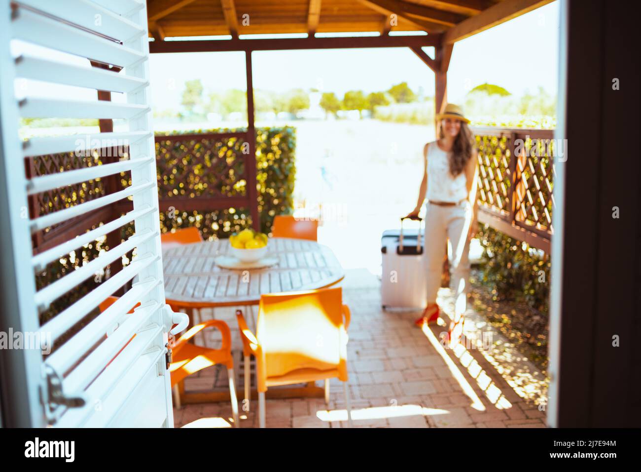 Closeup on door and woman with wheel bag in background in the patio of hotel guest house in the terrace. Stock Photo