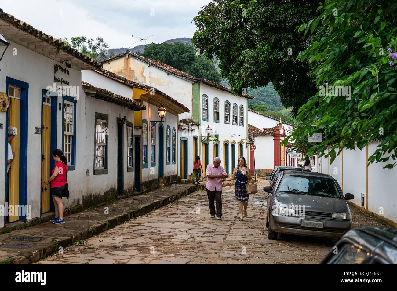 View of the Direita street with a row of colonial houses side by side and pedestrians walking by in Tiradentes historical center under clouded sky. Stock Photo