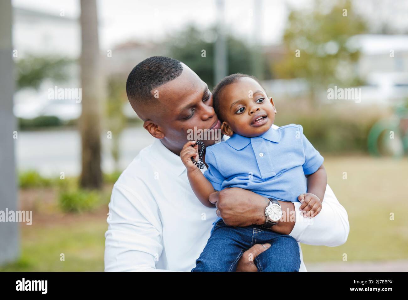 A dad holding his baby toddler boy and kissing him with affection on the cheek Stock Photo