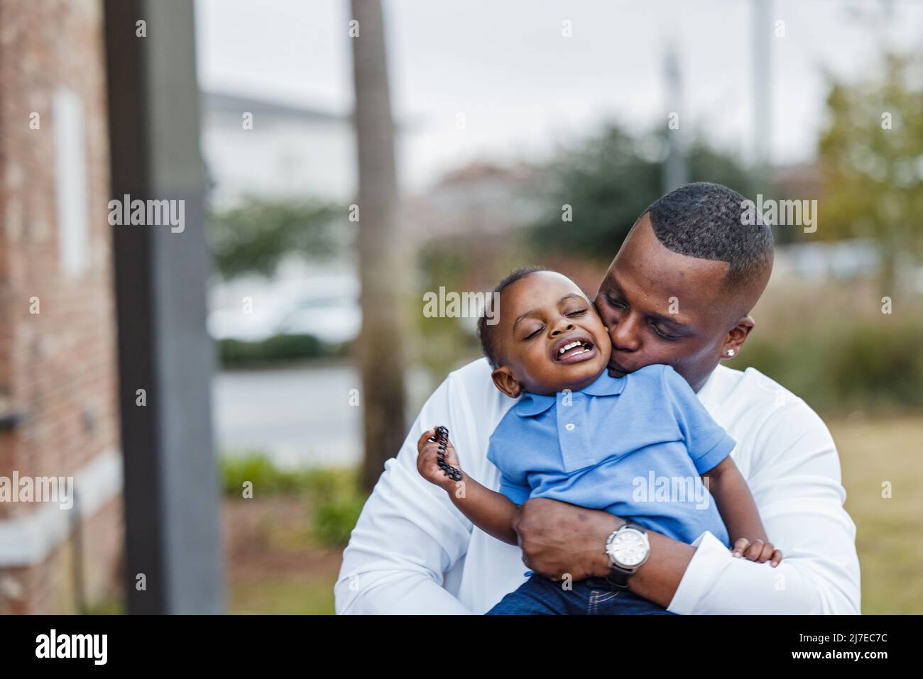 A dad holding his baby toddler boy and kissing him with affection on the cheek Stock Photo