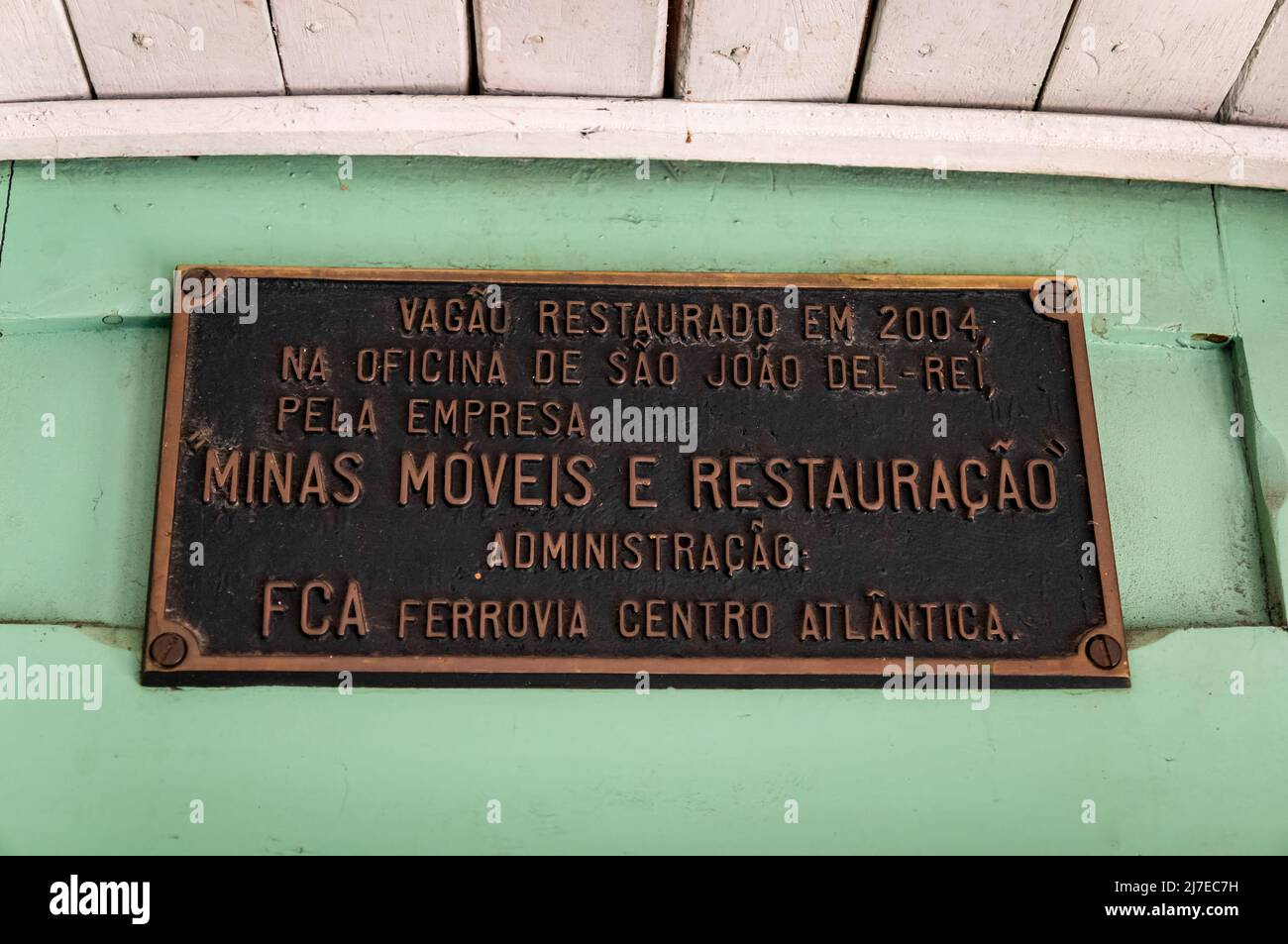 Metal information sign saying: 'Passenger car restored in 2004 at Sao Joao Del Rei workshops by Minas Moveis e Restauracao shop. Admin: FCA railway'. Stock Photo
