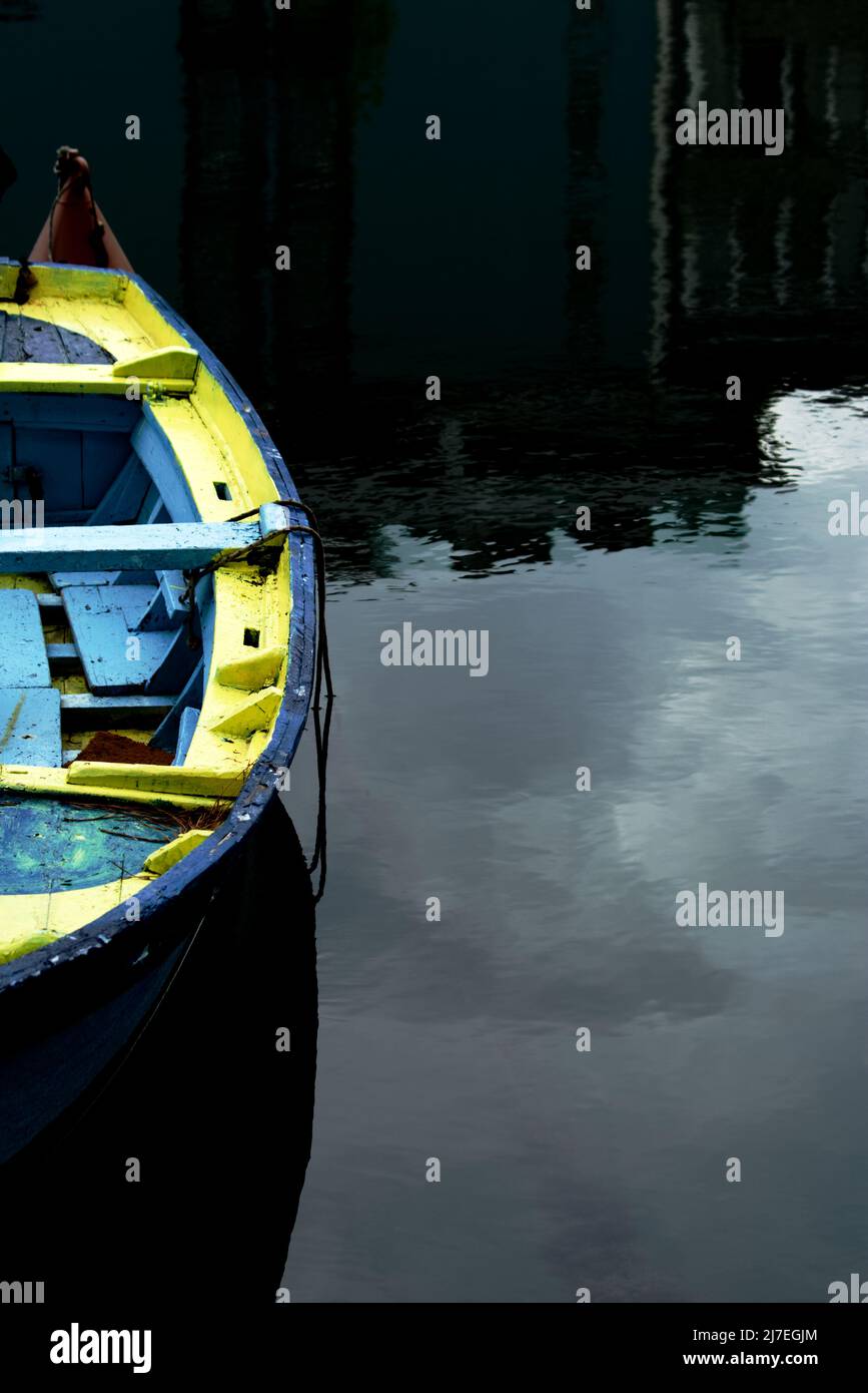 Blue and yellow wooden row boat on water reflecting the sky - colorful old row boat with a water reflection Stock Photo