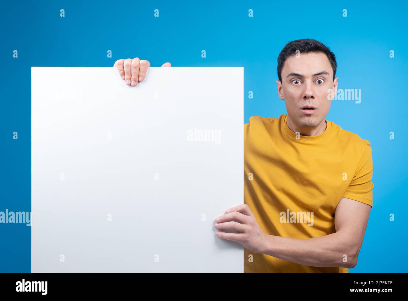 Startled guy showing white banner on blue background Stock Photo