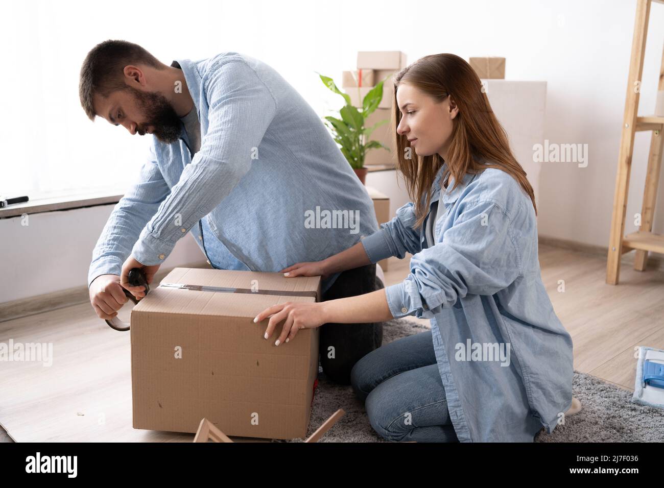 a man seals boxes ready for moving with scotch tape. couple in love packs things. Stock Photo