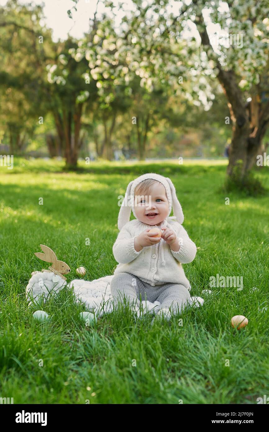 Easter Bunny baby boy. Egg hunting. Cute child in hat with ears and eggs on grass. Stock Photo