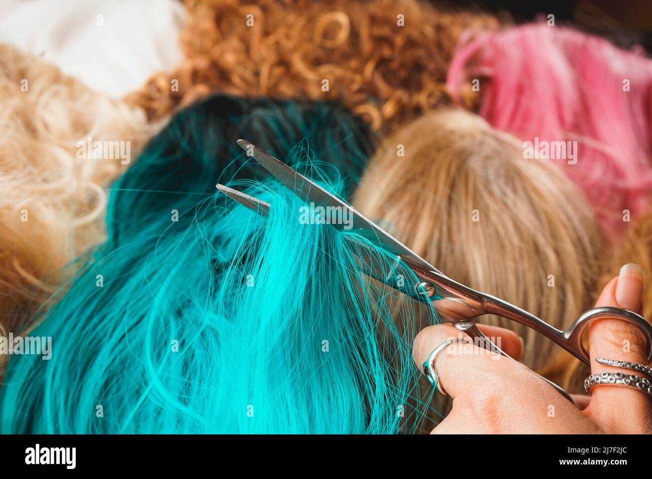 Cloose up of a hairdresser or a cosplayer cutting a blue wig to stylize it with a lot of different wigs as background Stock Photo