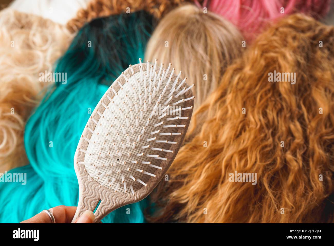 Close up of a hair brush against a background of a lot of wigs of different colors and styles Stock Photo
