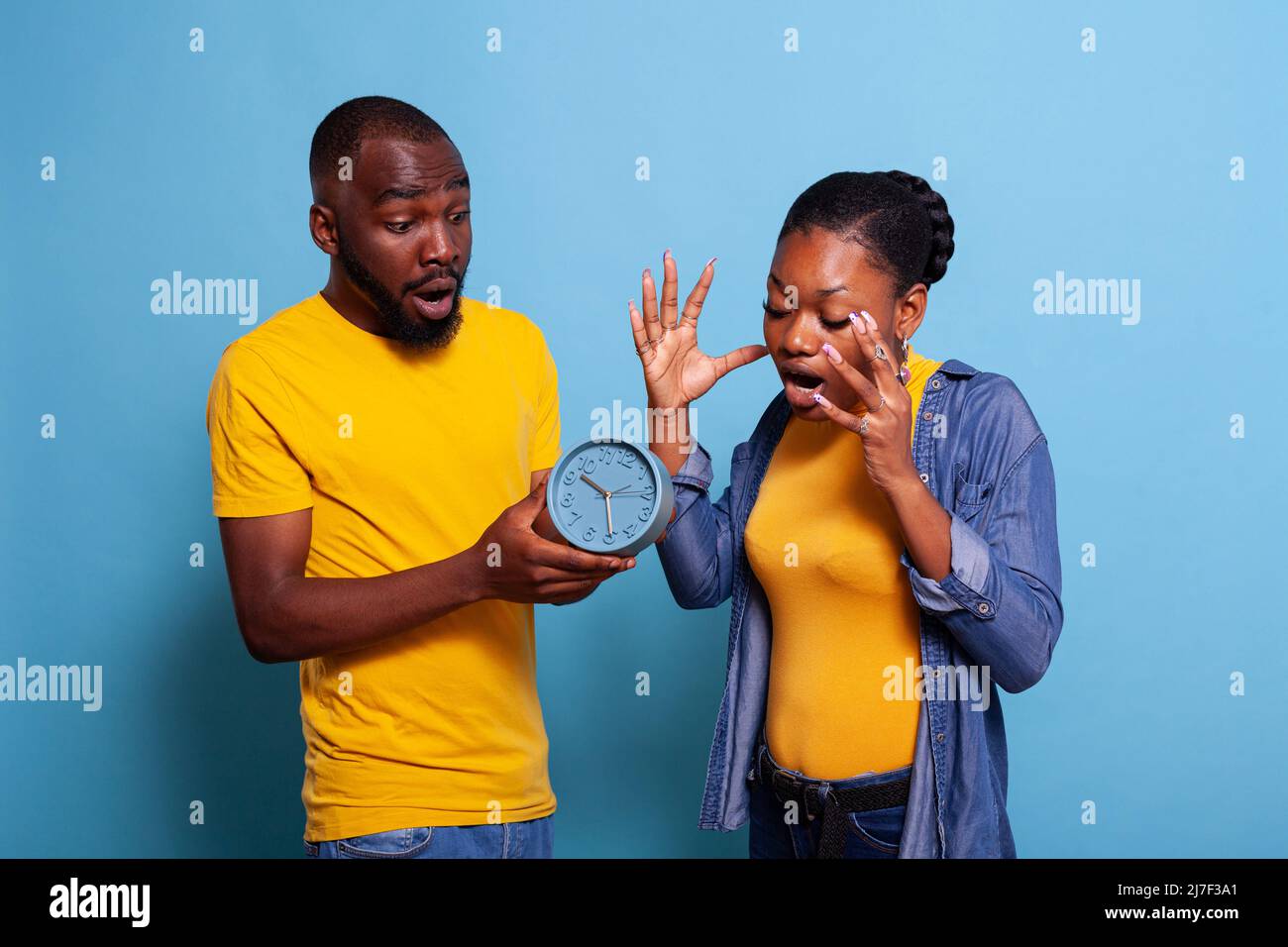 Stressed couple checking clock and running late to work, looking at time on watch. Impatient man and woman being in shock after deadline passing in studio. People following hour and minutes Stock Photo