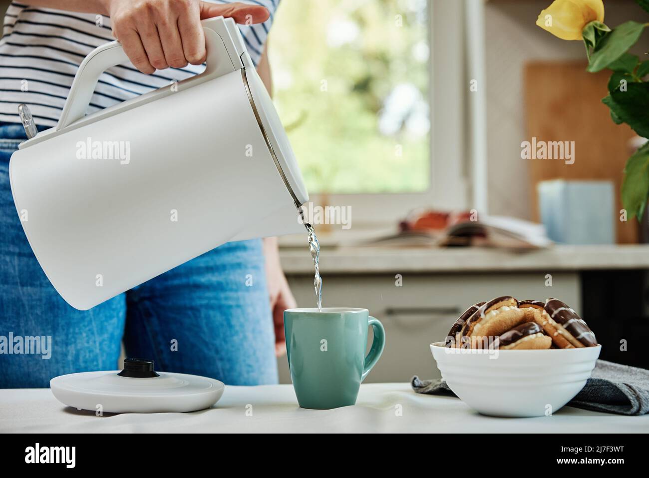 Tea time, Woman pouring boiled water from electric kettle into cup for