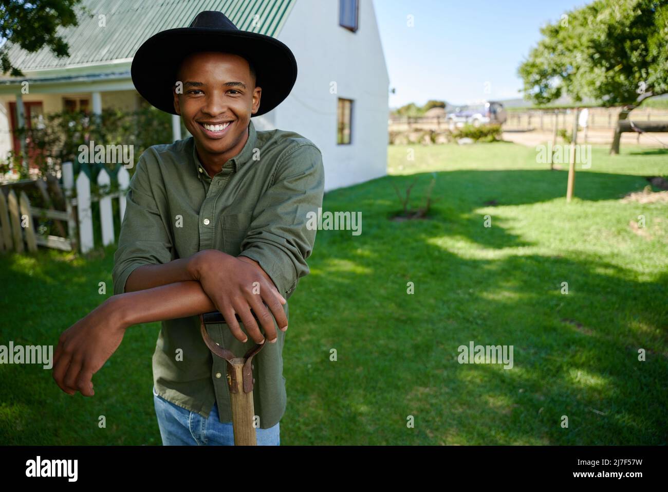 Mixed race male farmer standing in green field leaning on pitch fork  Stock Photo