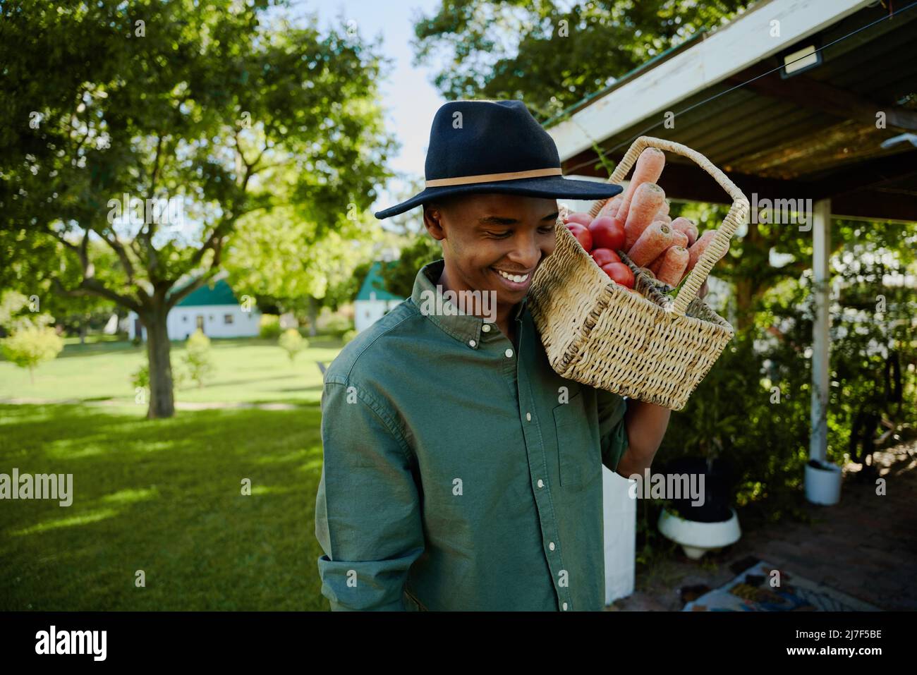 Mixed race male farmer walking through green fields with basket of fresh vegetables  Stock Photo