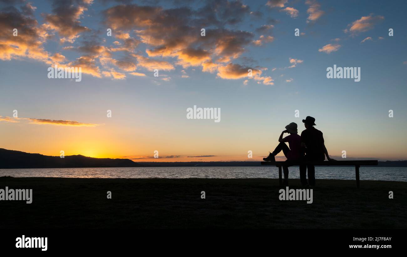 Silhouette image of a couple sitting on a bench and watching sunset, Rotorua, New Zealand. Stock Photo
