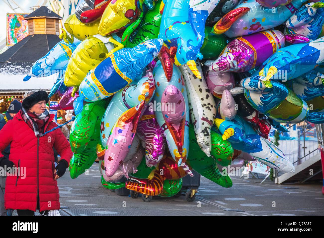 London, UK - 28 November, 2021 - Female street vendor sells multiple cartoon character helium balloons at Christmas funfair Hyde Park Winter Wonderlan Stock Photo