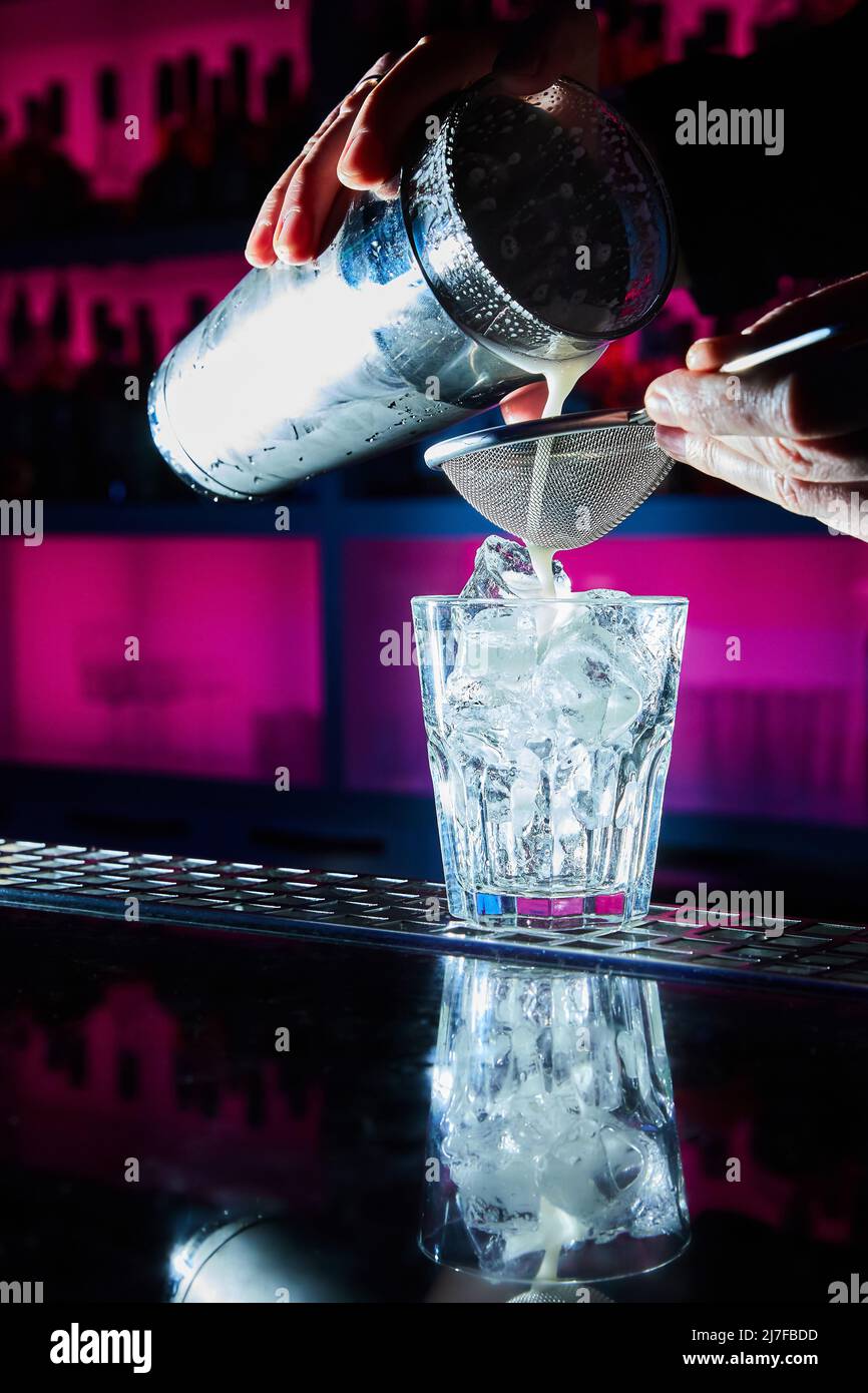 The bartender prepares a cocktail on the bar counter using a shaker and