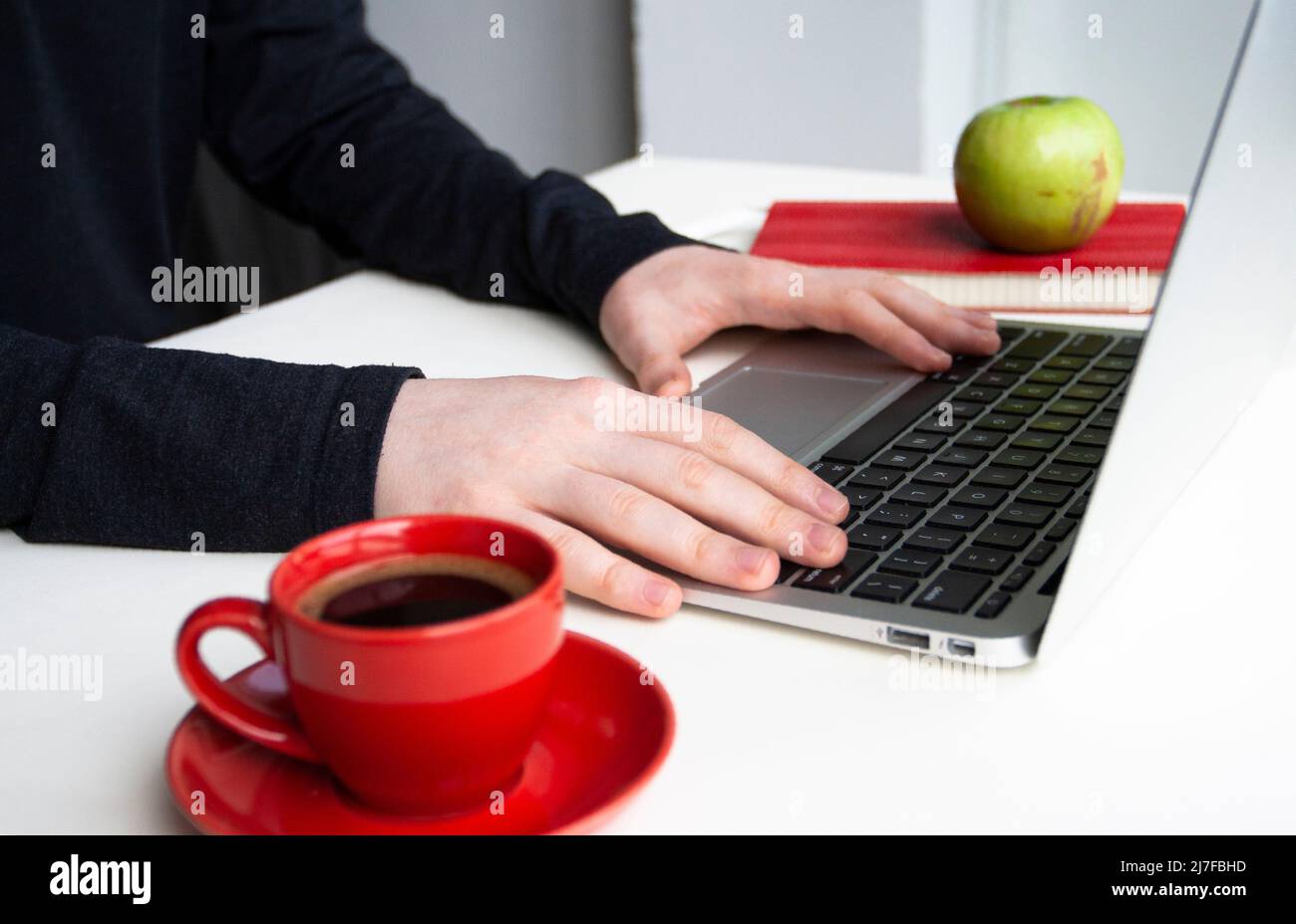 Man hands in lay on keyboard and mouse with red cup of coffee, notebooks, headhones and glasses case on white table Stock Photo
