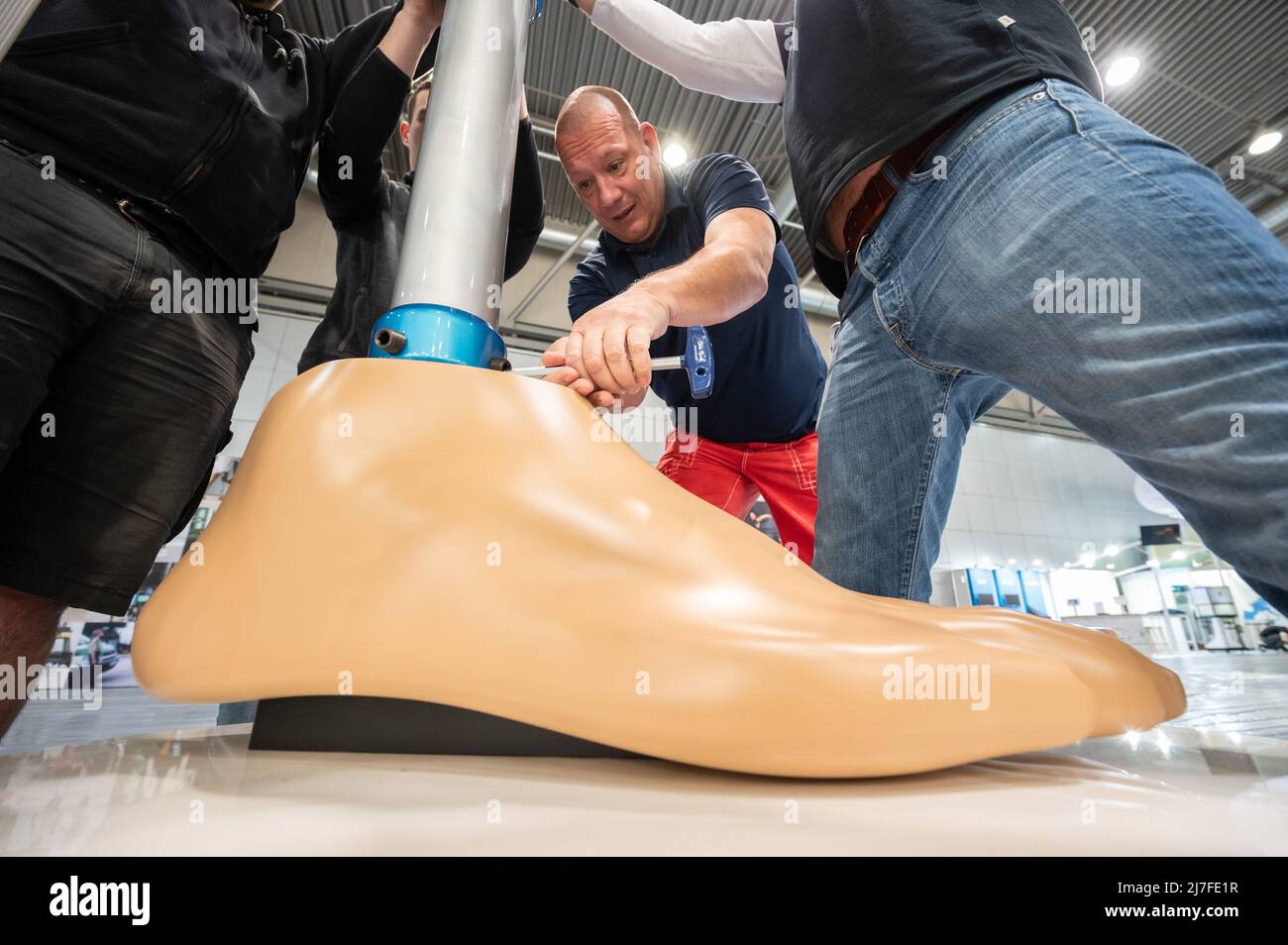 Leipzig, Germany. 09th May, 2022. Mathias Börner, (M) Ottobock sales representative for Saxony and Thuringia, screws on an oversized model of a leg prosthesis. To mark the 25th anniversary of the C-Leg leg prosthesis, the Duderstadt-based company Ottobock is displaying a four-meter-high model of it at OTWorld 2022, the world's leading trade fair for orthopaedic and rehabilitation technology. It was the world's first mechatronic knee joint. The C-Leg technology has now been used in more than 100,000 fittings worldwide. Credit: Christian Modla/dpa/Alamy Live News Stock Photo