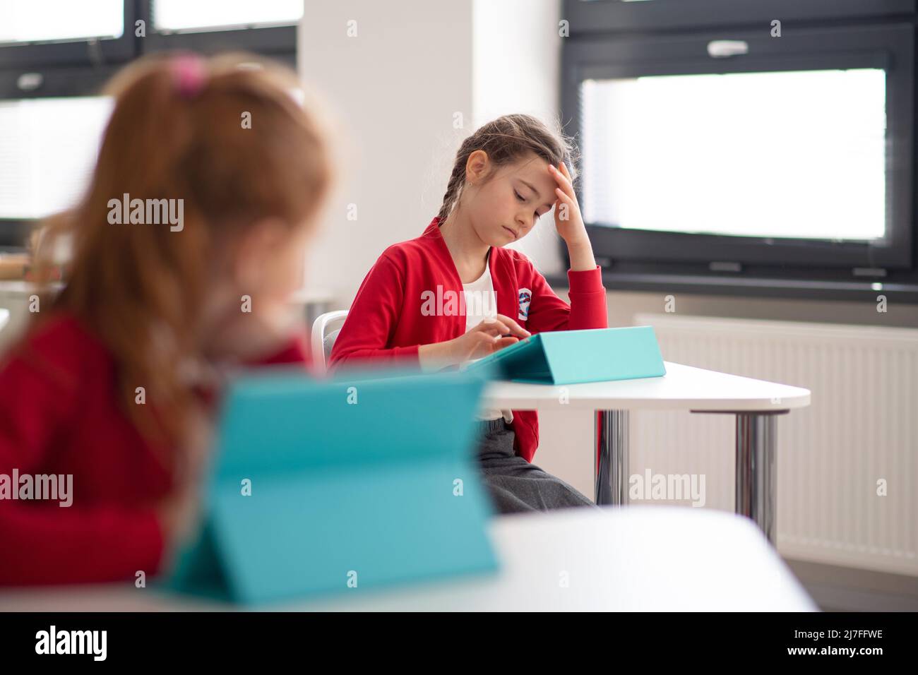 Bored schoolgirl using digital tablet during lesson in classroom at primary school. Stock Photo