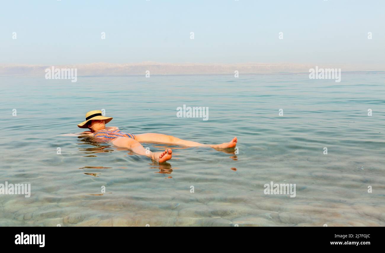 Blonde woman with hat floating in the turquoise waters of the Dead Sea Stock Photo