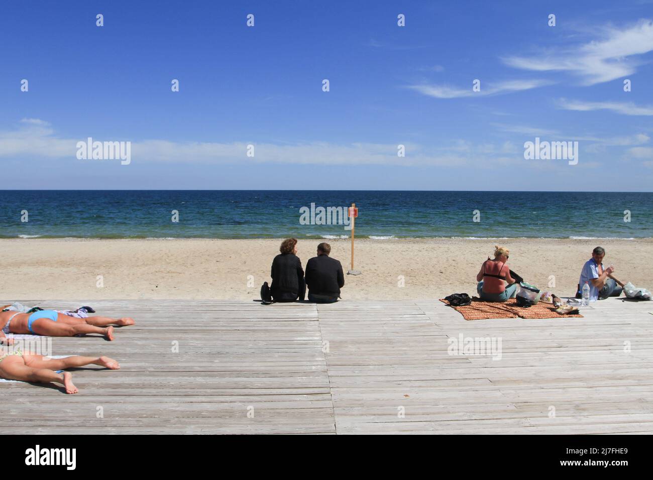 People sunbathing at Dolphin Beach near a 'careful mines' sign. The