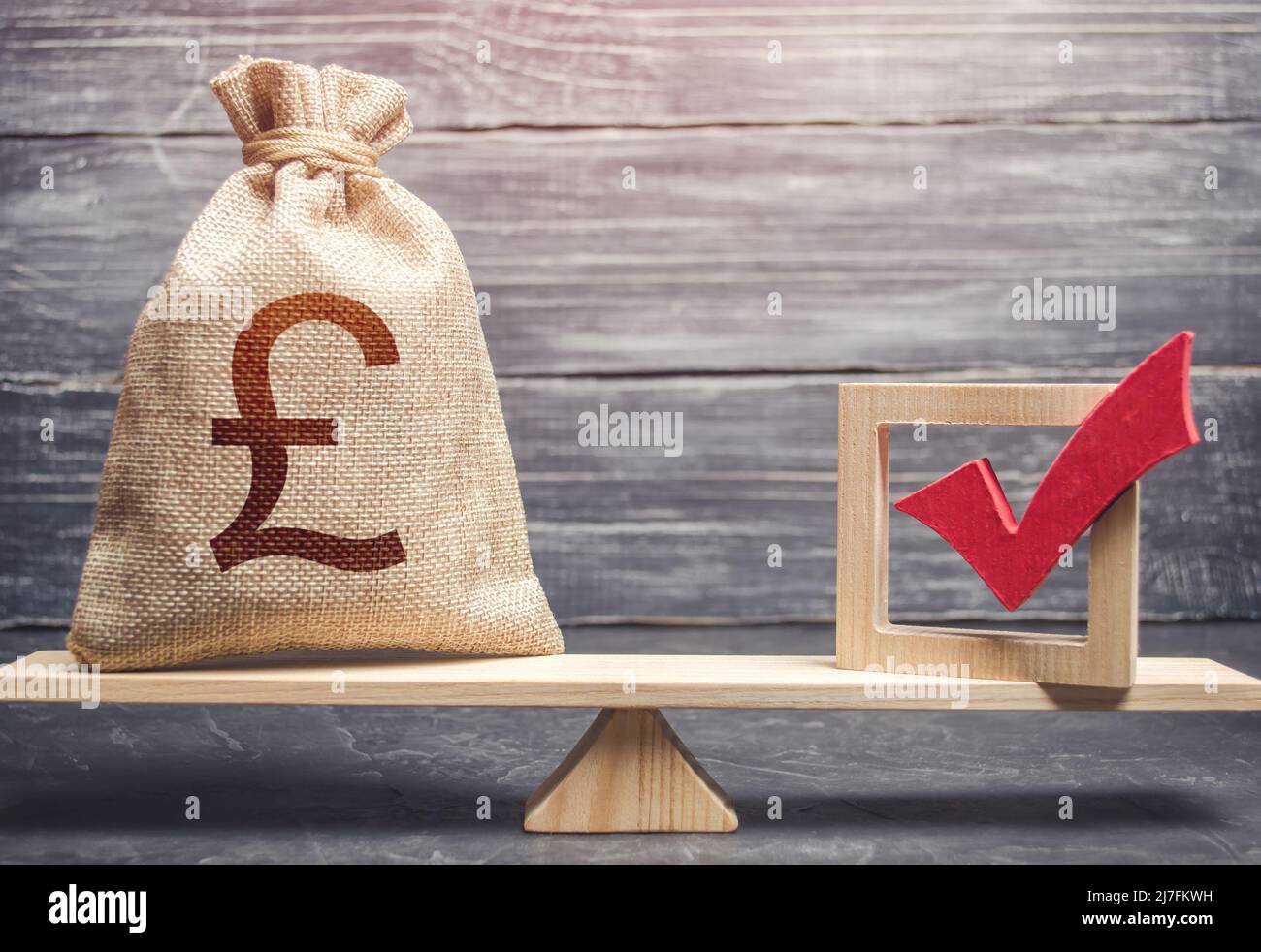 Red vote tick and a british pound sterling money bag on scales. Estimating cost of making a decision and consequences in the future. Corruption risks. Stock Photo