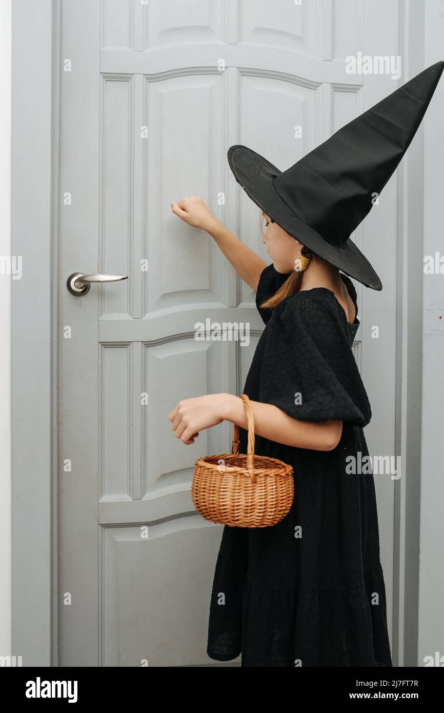 Little girl in a witch costume knocking on the door, trick or treating. Her eyes closed, gathering her courage. Stock Photo