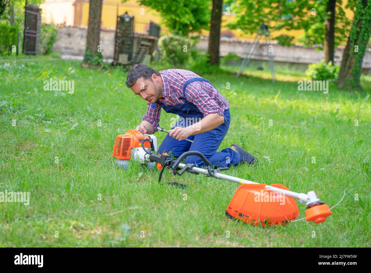 One gardener mowing grass fixing brush cutter problem Stock Photo
