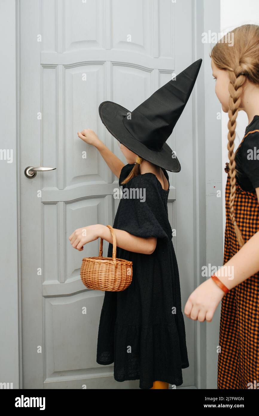 Girl friends in halloween costumes knocking on the door, trick or treating. Her eyes closed, gathering her courage. Stock Photo