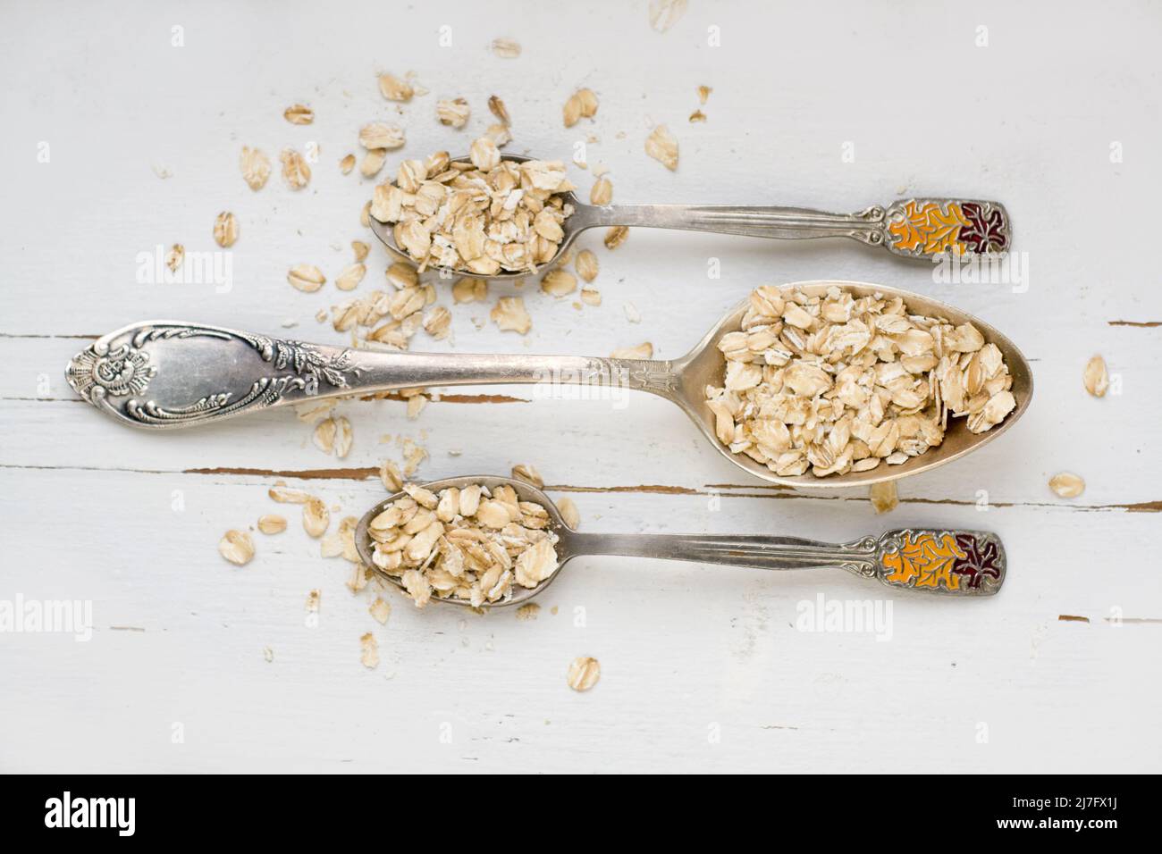 Three tablespoons of oatmeal lying on a white wooden background ...