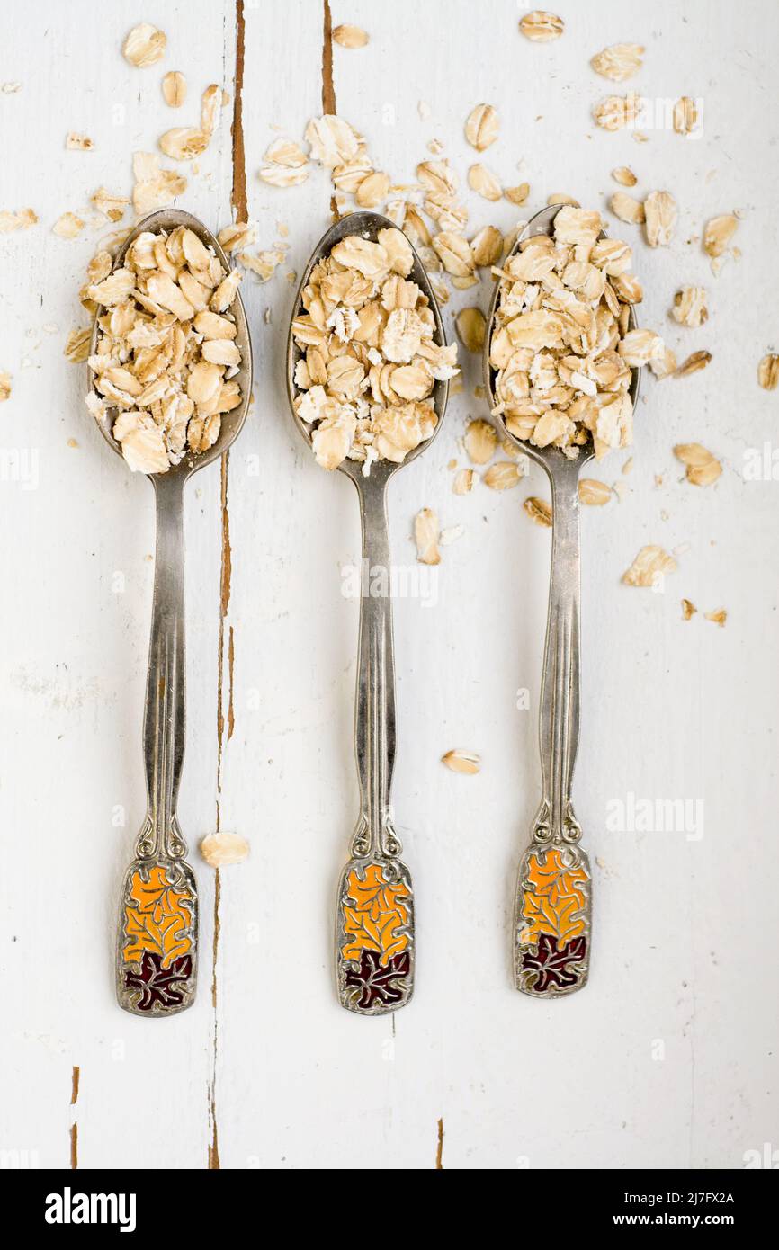 Three tablespoons of oatmeal lying on a white wooden background ...