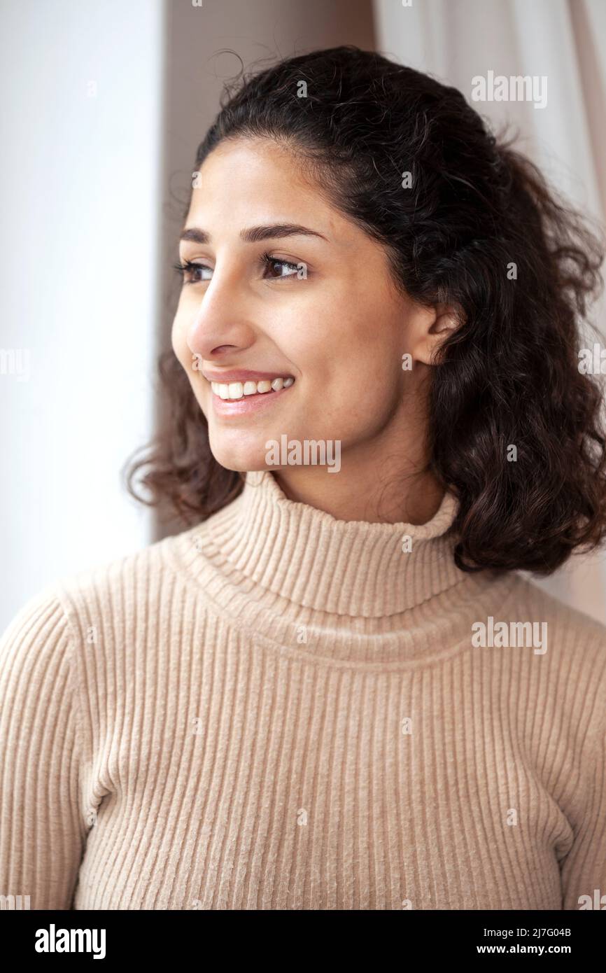 Smiling young woman looking through window Stock Photo