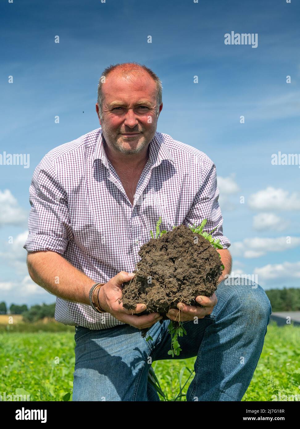 Farmer looking at soil structure in a trial plot, looking at how to