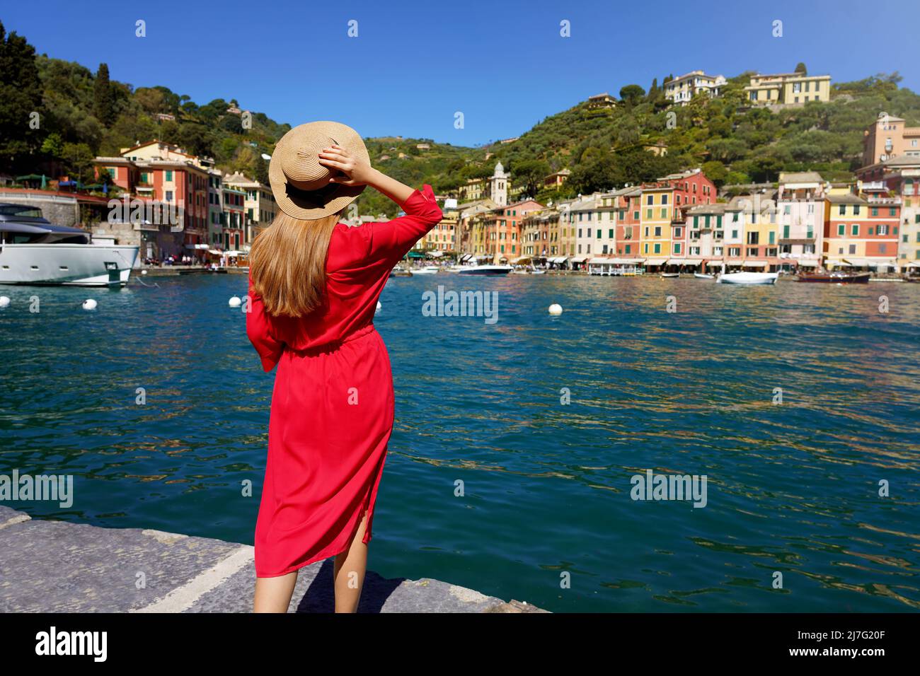 Holidays in Italy. Rear view of beautiful young woman in red dress looks towards Portofino traditional colorful village with yachts moored in its pict Stock Photo
