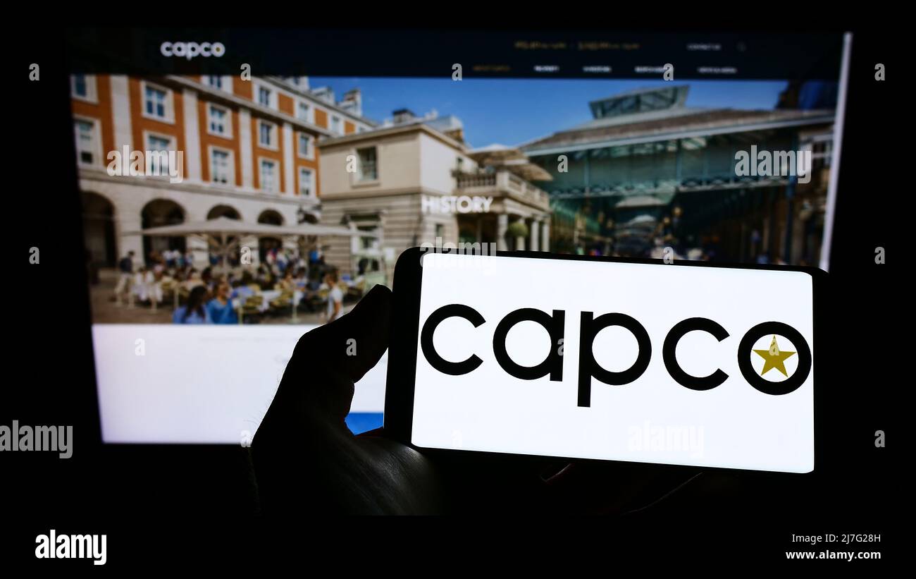 Person holding cellphone with logo of company Capital Counties Properties plc (Capco) on screen in front of webpage. Focus on phone display. Stock Photo