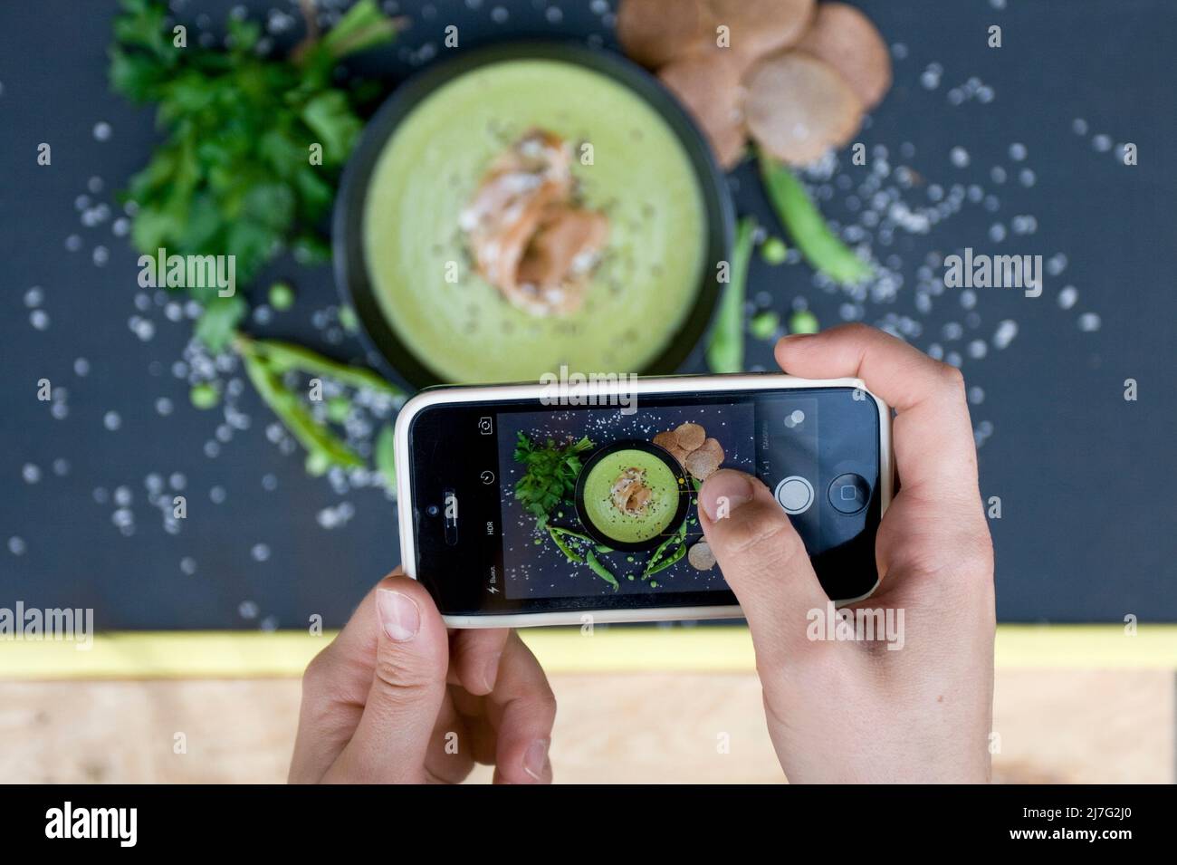 The girl photographed her lunch on a smartphone. Soup with green peas and buckwheat chips, top view. Stock Photo