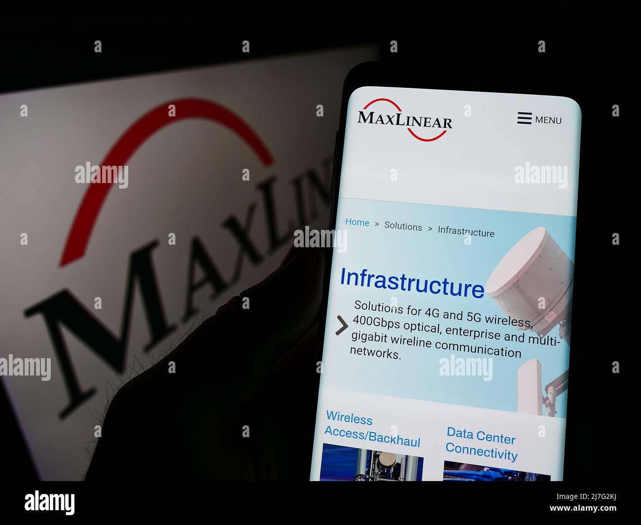 Person holding cellphone with webpage of American hardware company MaxLinear Inc. on screen in front of logo. Focus on center of phone display. Stock Photo