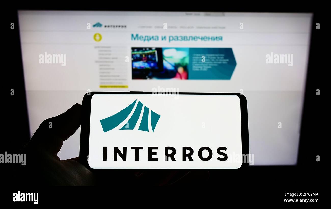 Person holding cellphone with logo of Russian conglomerate Interros on screen in front of business webpage. Focus on phone display. Stock Photo