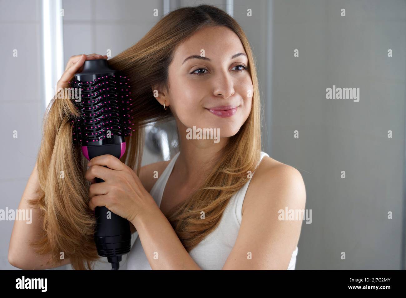 Girl using brush hair dryer to style hair at the mirror on bathroom