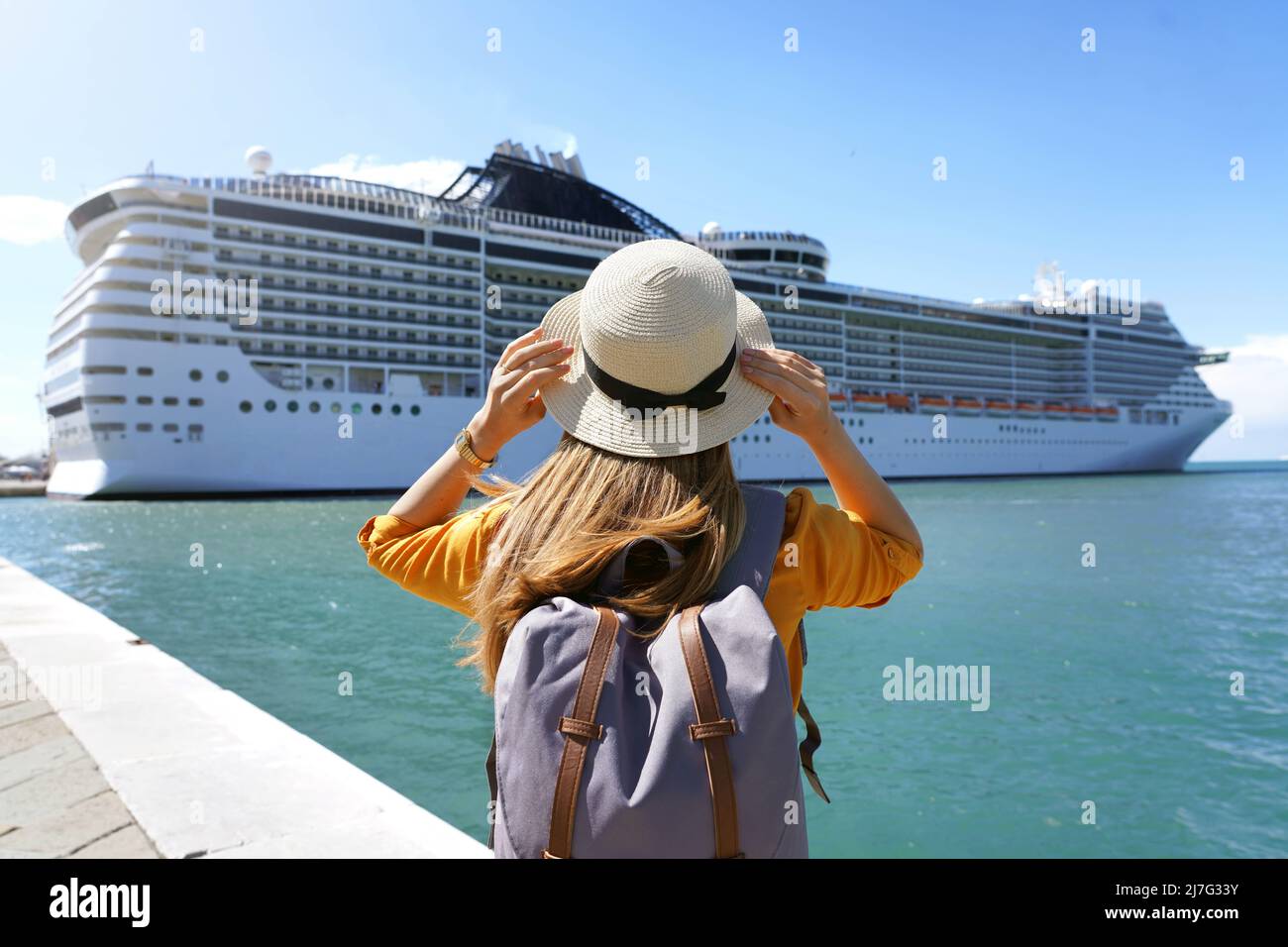 Tourist girl with backpack and hat standing in front of big cruise liner Stock Photo