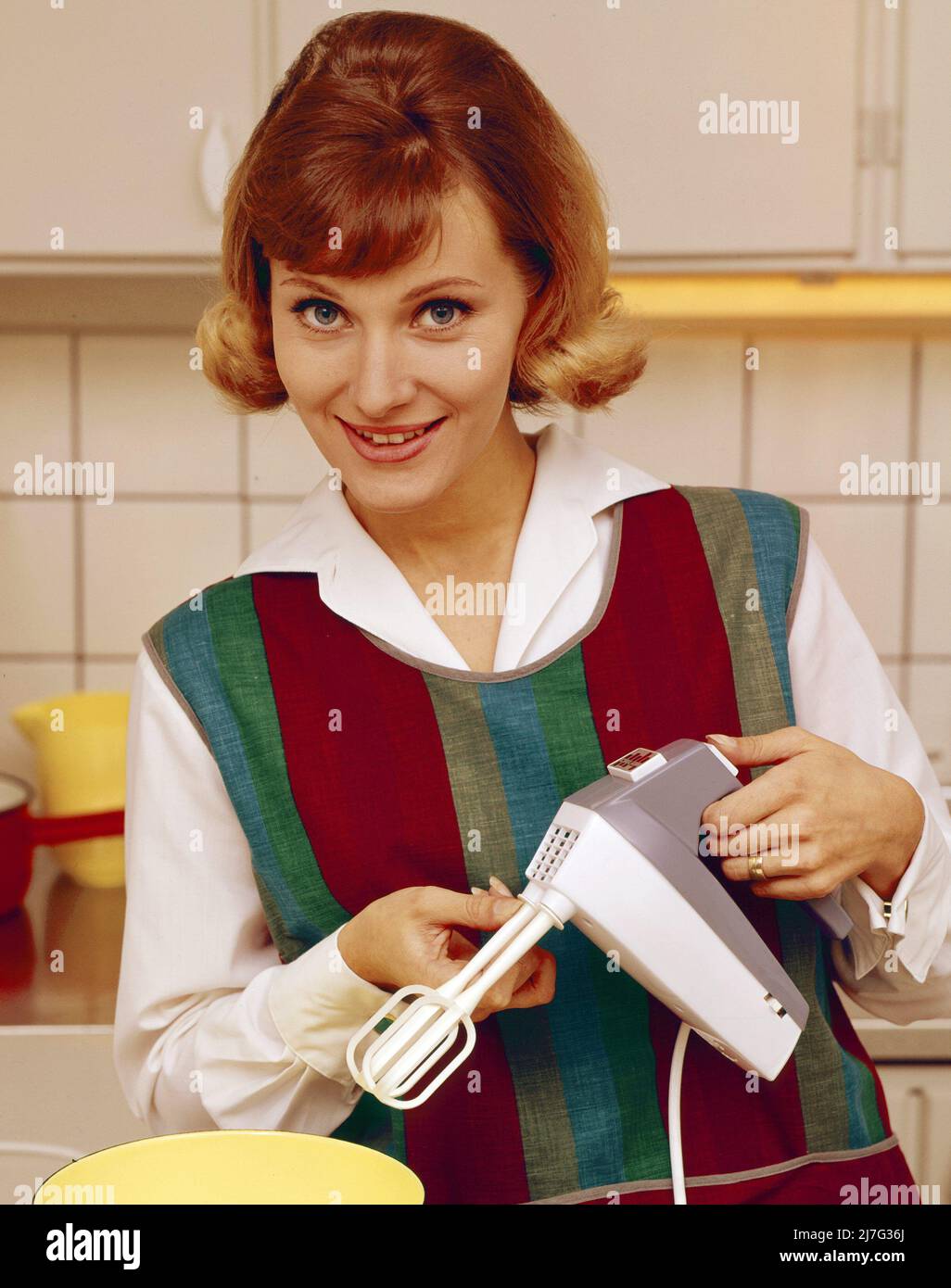 In the 1960s. A young woman pictured in the kitchen using an electric hand mixer. Stock Photo
